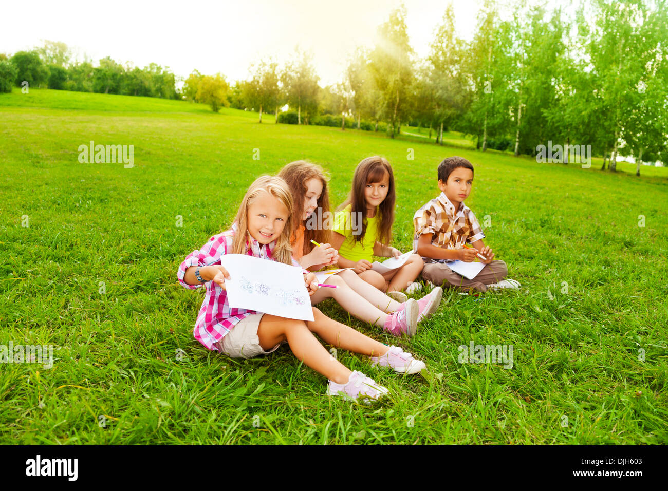 Four little 6 and 7 years old kids sitting in the grass and drawing pictures  Stock Photo