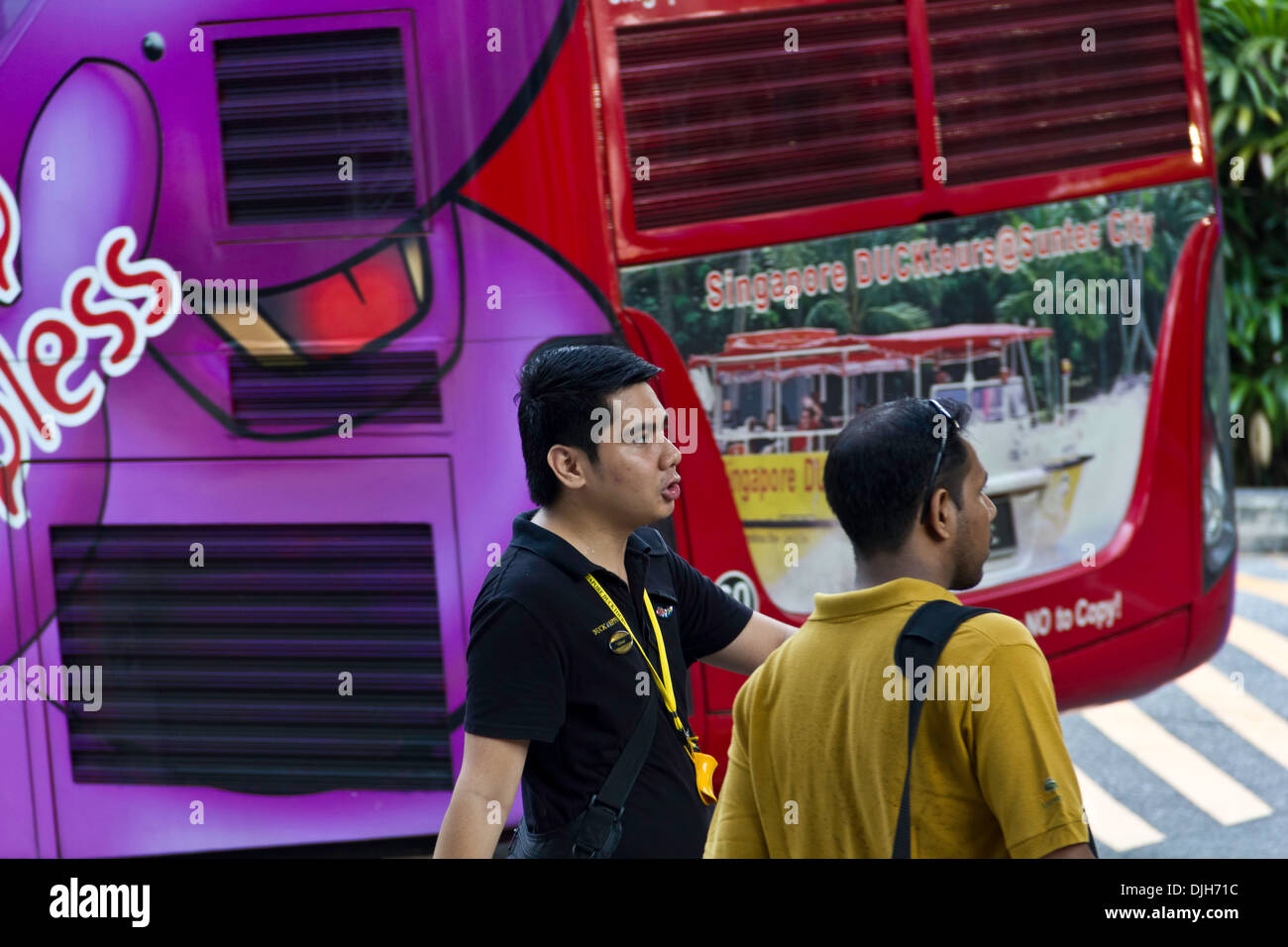 2 men near the back of a tour bus used for different city tours in Singapore, with one being a tourist and the other a guide Stock Photo