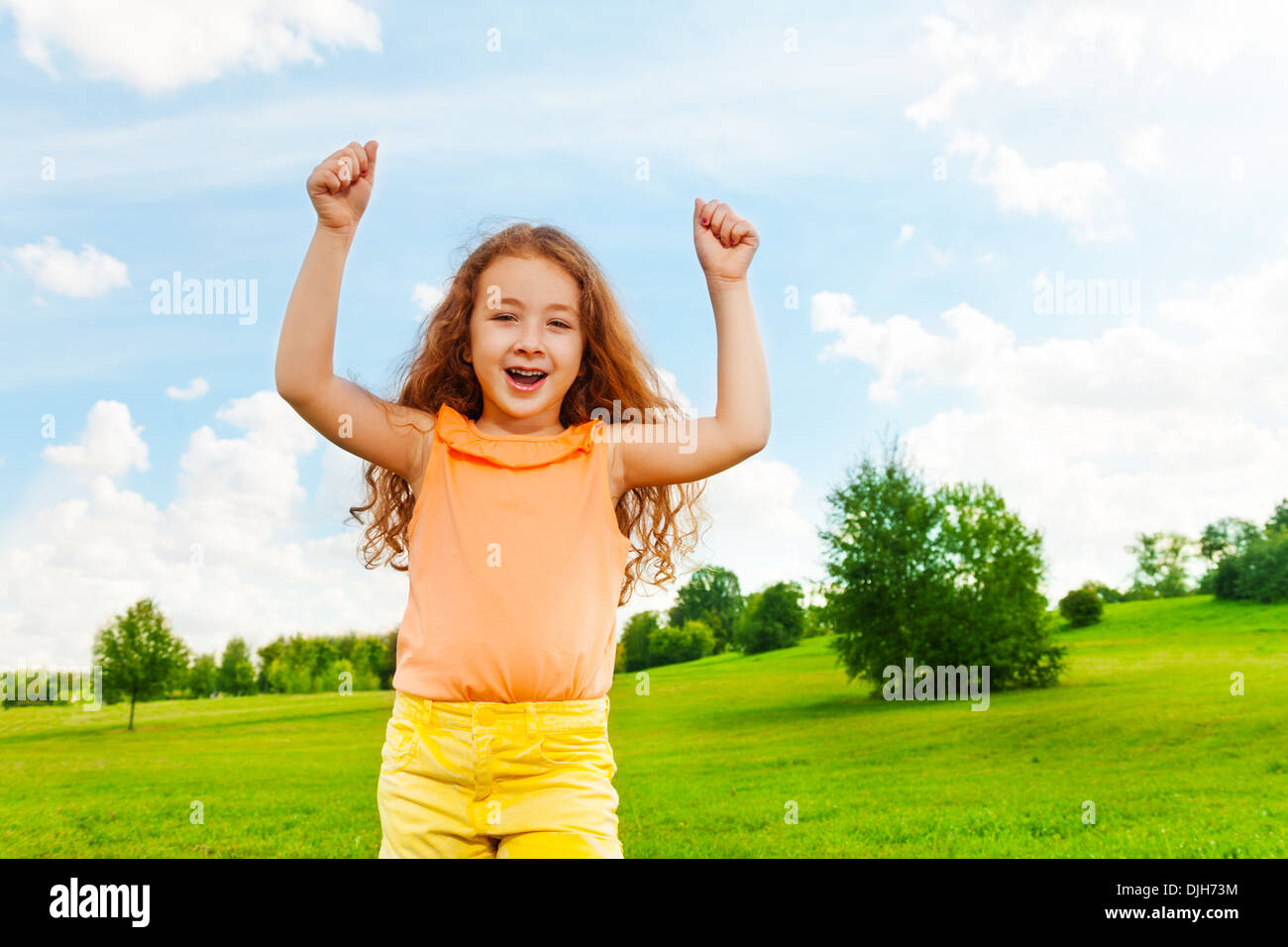 Happy little girl with long hair and lifted hands standing in the park Stock Photo