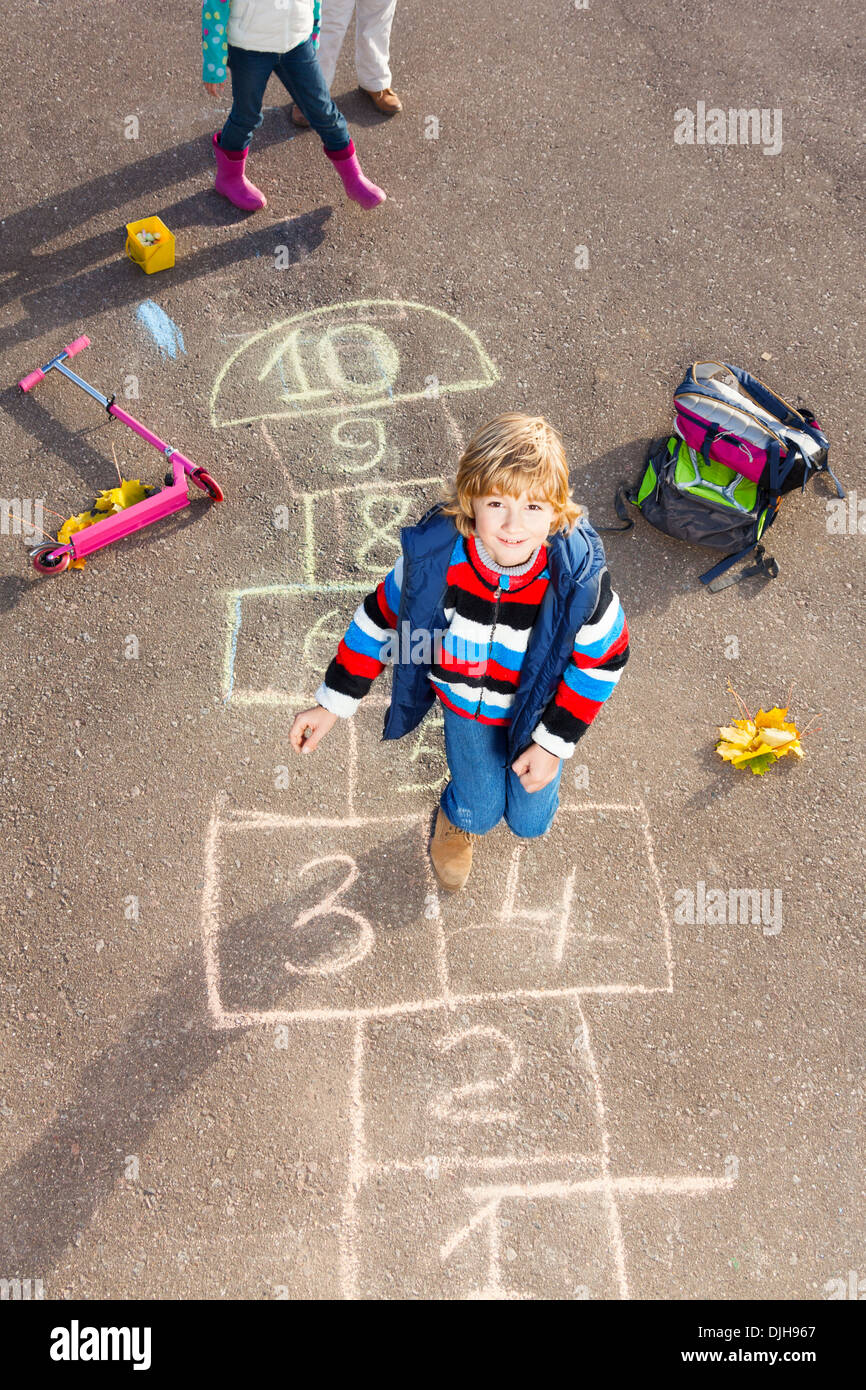 Boy jumping on the hopscotch game drawn on the asphalt looking up