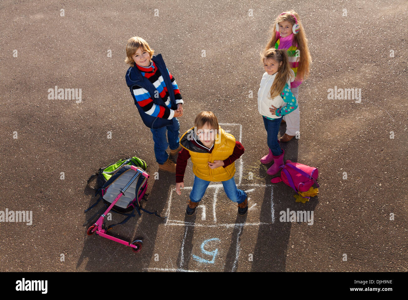 Happy boy jumping on hopscotch game with friends boys an girls standing by  with school bags laying near Stock Photo - Alamy