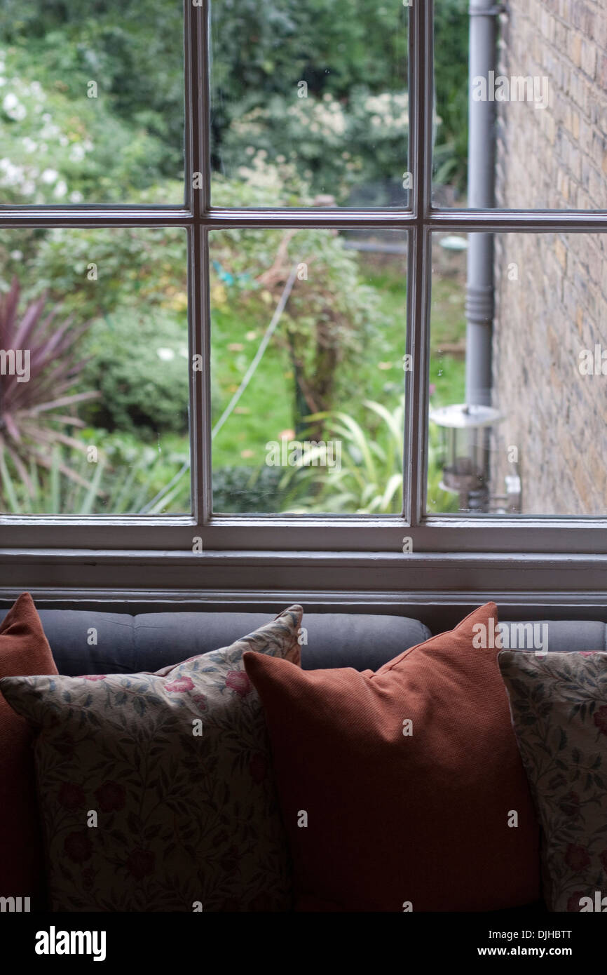 A calm view over cushions on a sofa through a sash window to a cottage garden Stock Photo