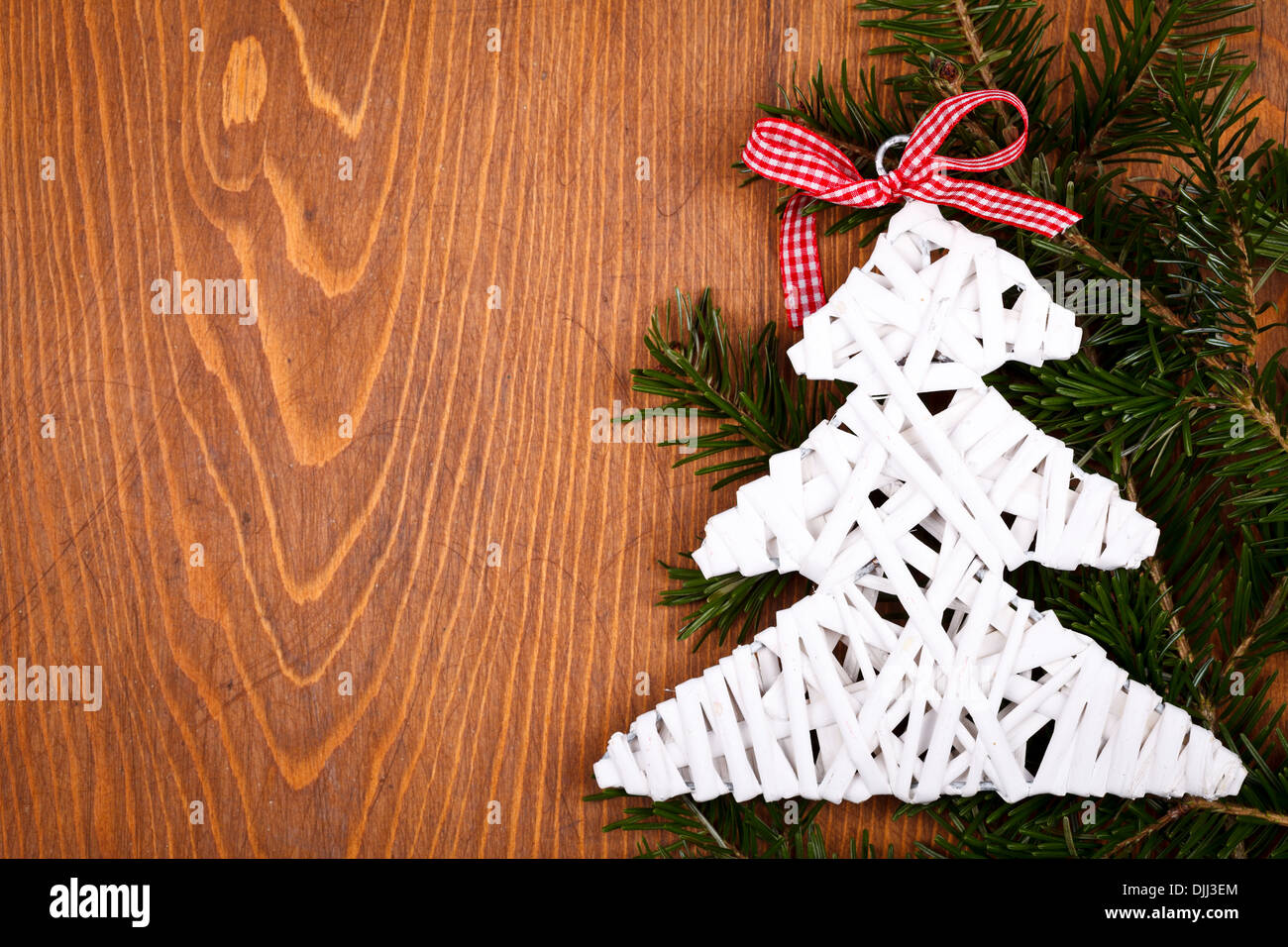 Little white Christmas tree with red ribbon on juniper leaves over wooden background Stock Photo