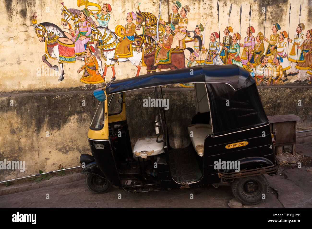 A rickshaw is parked next to a wall decorated with drawings representing the time of the ancient maharajahs. Stock Photo