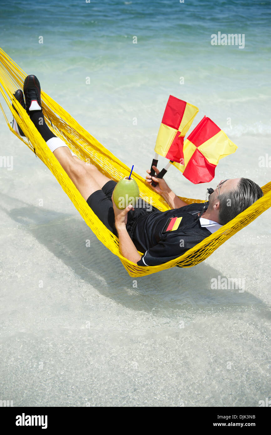 Soccer football referee takes a break from the World Cup to relax at the beach in hammock with coconut Stock Photo