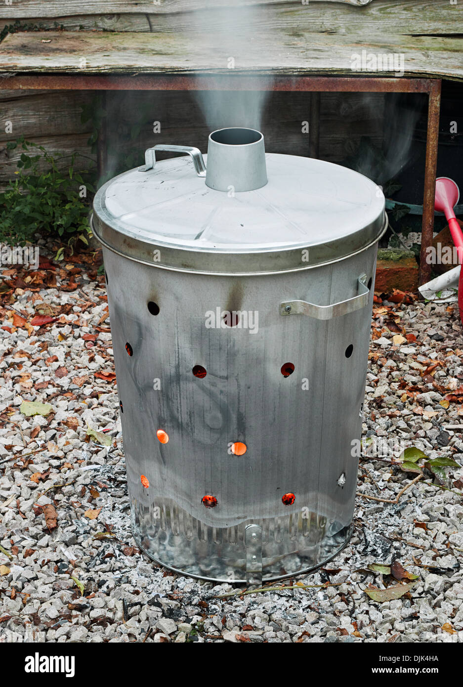Garden incinerator bin burning garden waste with smoke coming out of the flue Stock Photo