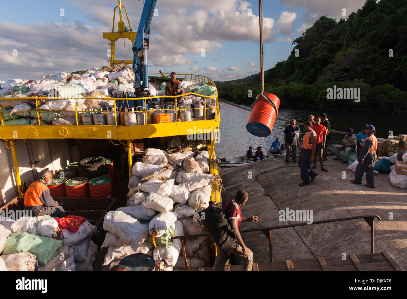 A crane unloading large drums of petrol (premix) from the irregular supply boat Lady Sandy onto the wharf. Lomati,  Matuku Fiji Stock Photo