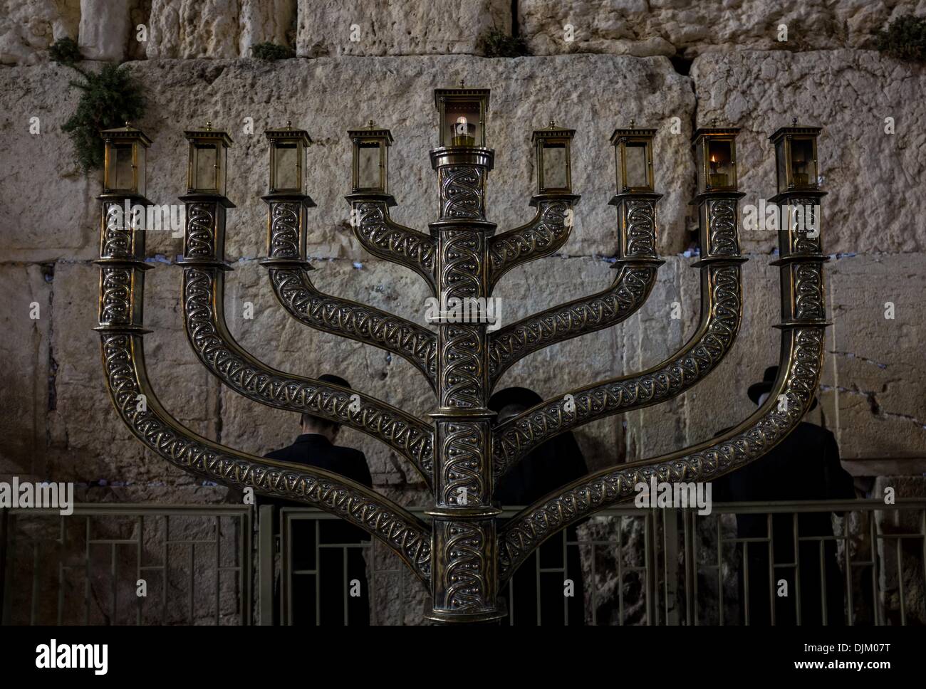 Orthodox Jews pray to mark Hanukkah behind a large-sized Hannukiya at the Western Wall in the Old City of Jerusalem, on Nov. 28, 2013. Hanukkah, also known as the Festival of Lights and Feast of Dedication, is an eight-day Jewish holiday commemorating the rededication of the Holy Temple (the Second Temple) in Jerusalem at the time of the Maccabean Revolt against the Seleucid Empire of the 2nd Century B.C. Hanukkah is observed for eight nights and days, starting on the 25th day of Kislev according to the Hebrew calendar, which may occur at any ti Stock Photo