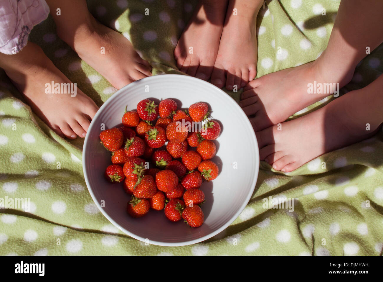 three girls feet standing next to a white bowl of strawberries, strawberry little pink toes in Somerset, UK. Stock Photo