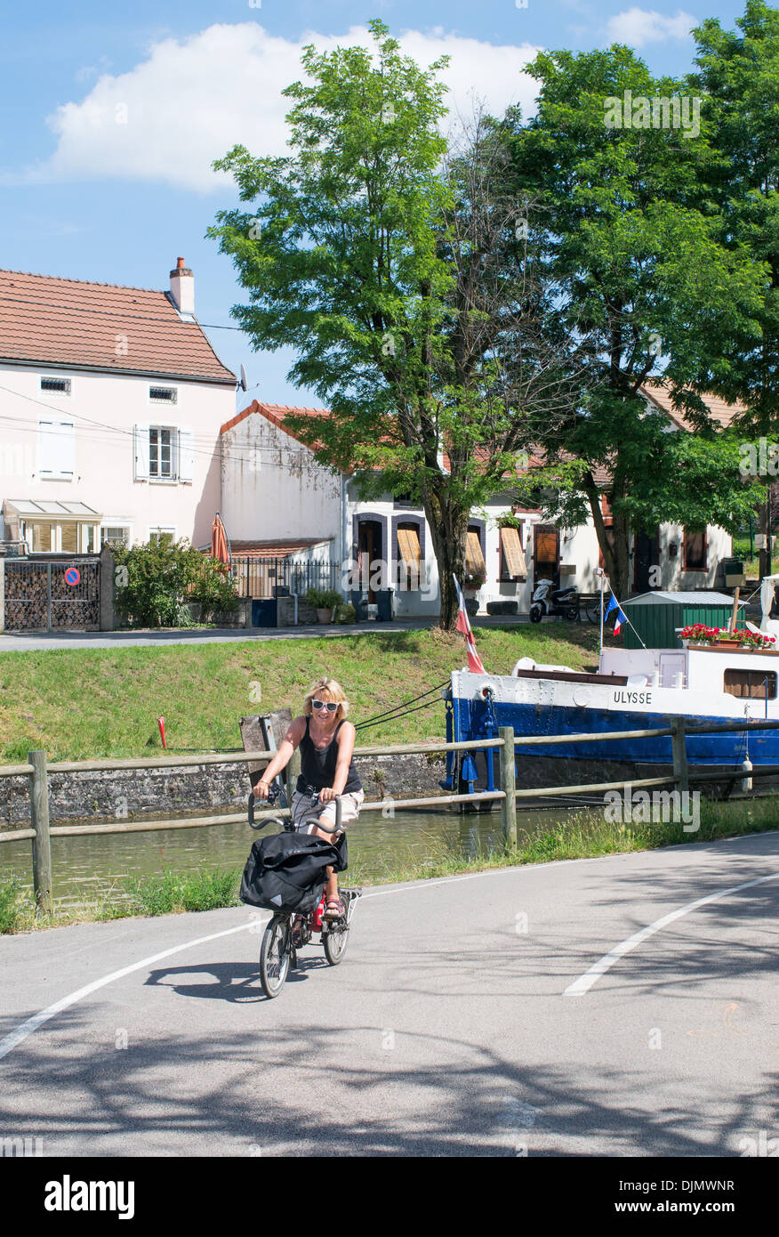 Female cyclist rides along the canal towpath within Chagny eastern France Stock Photo