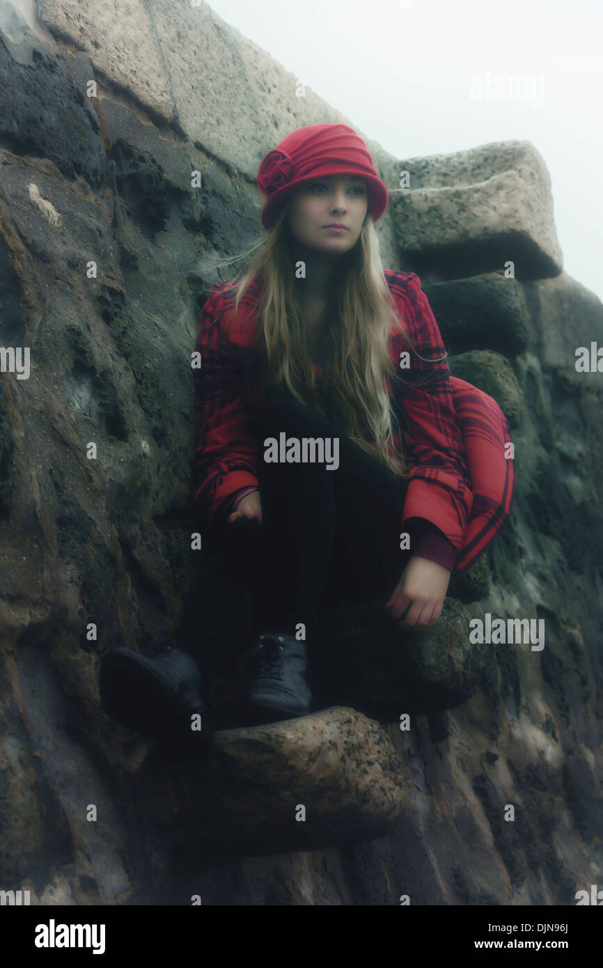 a girl in a red coat with a hat is sitting on old stone stairs Stock Photo