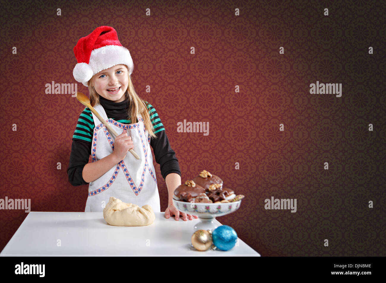 little girl making xmas cookies in front of red background Stock Photo