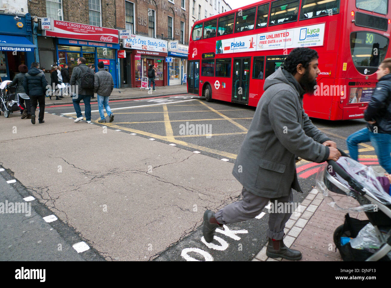Pedestrians man pram crossing busy road Grays Inn Road with red double decker bus buses cars traffic in King's Cross area of London UK  KATHY DEWITT Stock Photo
