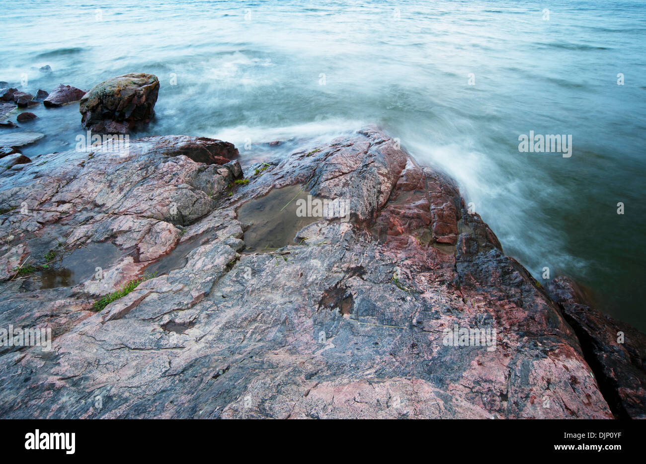 Long exposure of waves crashing into rocks at shore line Stock Photo