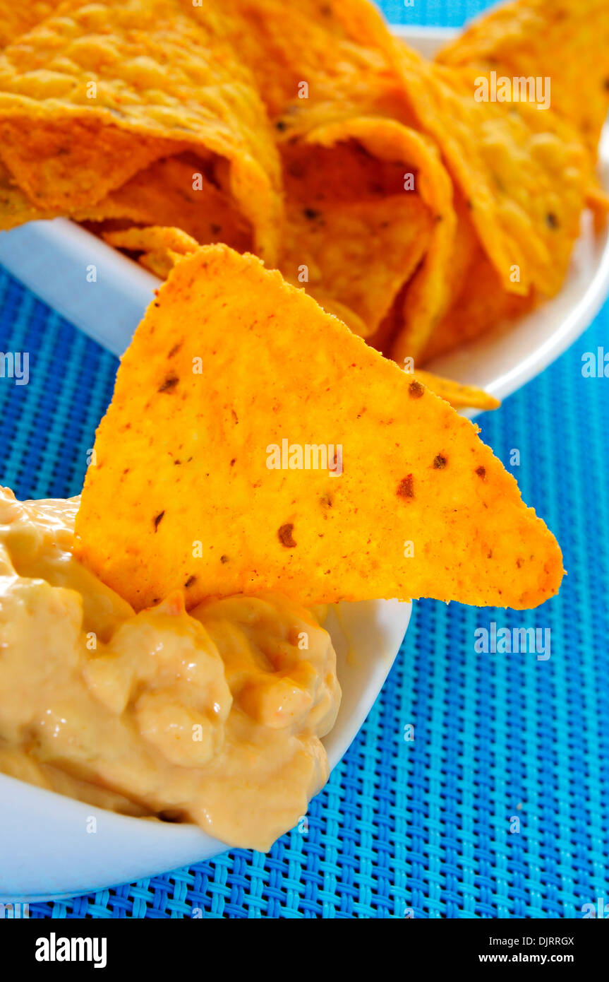 closeup of a bowl with tortilla chips dipped in nacho cheese on a blue background Stock Photo