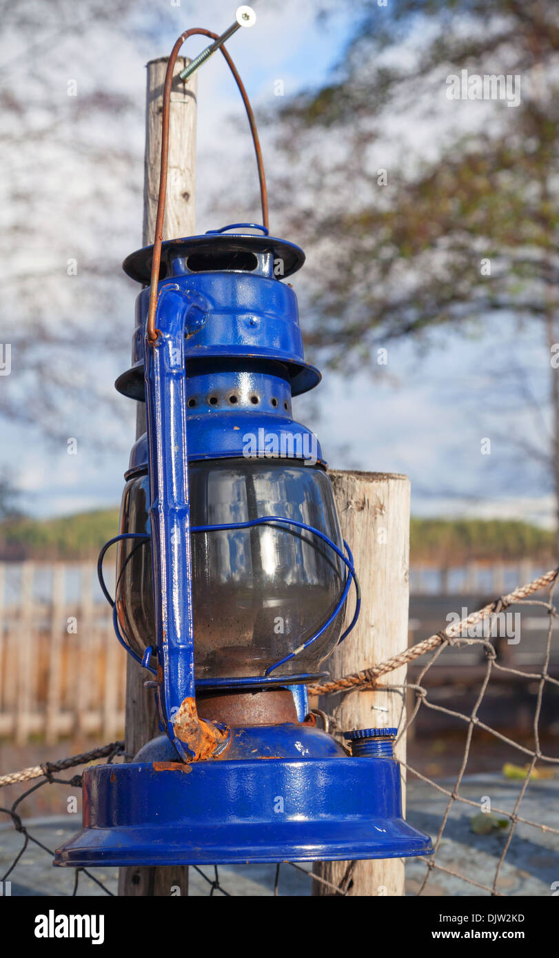 Blue vintage kerosene lamp hangs on old outdoor fence Stock Photo