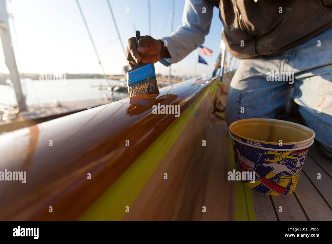 A varnisher varnishes a teak cap rail on a sailing yacht at Newport