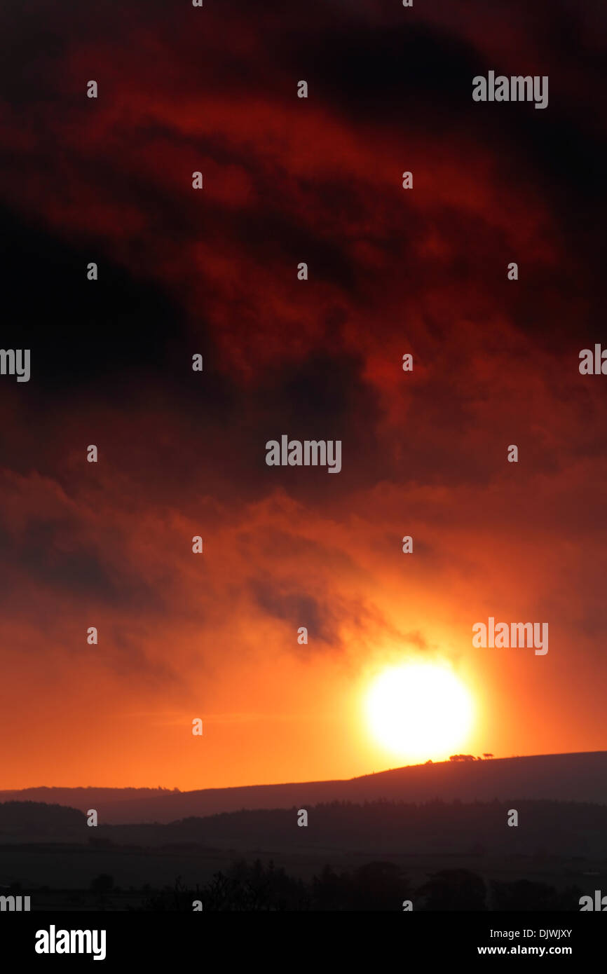 Sun rising over rolling hills into a colourful fiery stormy sky. Stock Photo