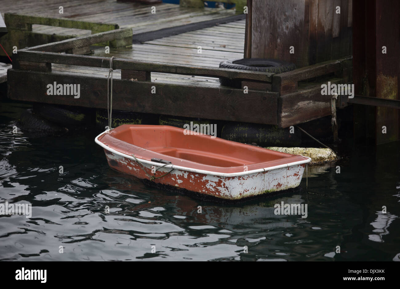 Small weathered dinghy tied to a dock. Stock Photo