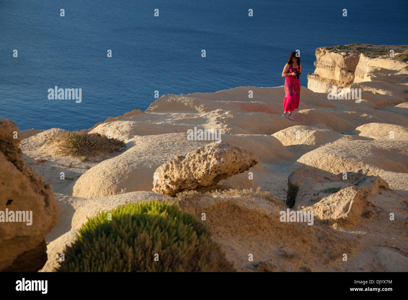 A woman strolling on a plateau eroded into waves by wind erosion in western Gozo seacliffs. Stock Photo