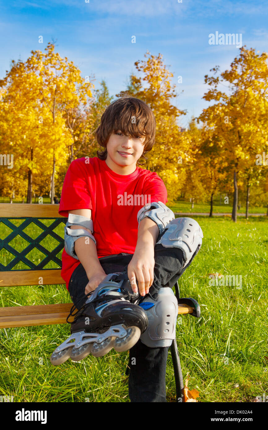 Happy 12 years old boy in red shirt sitting on bench and putting on