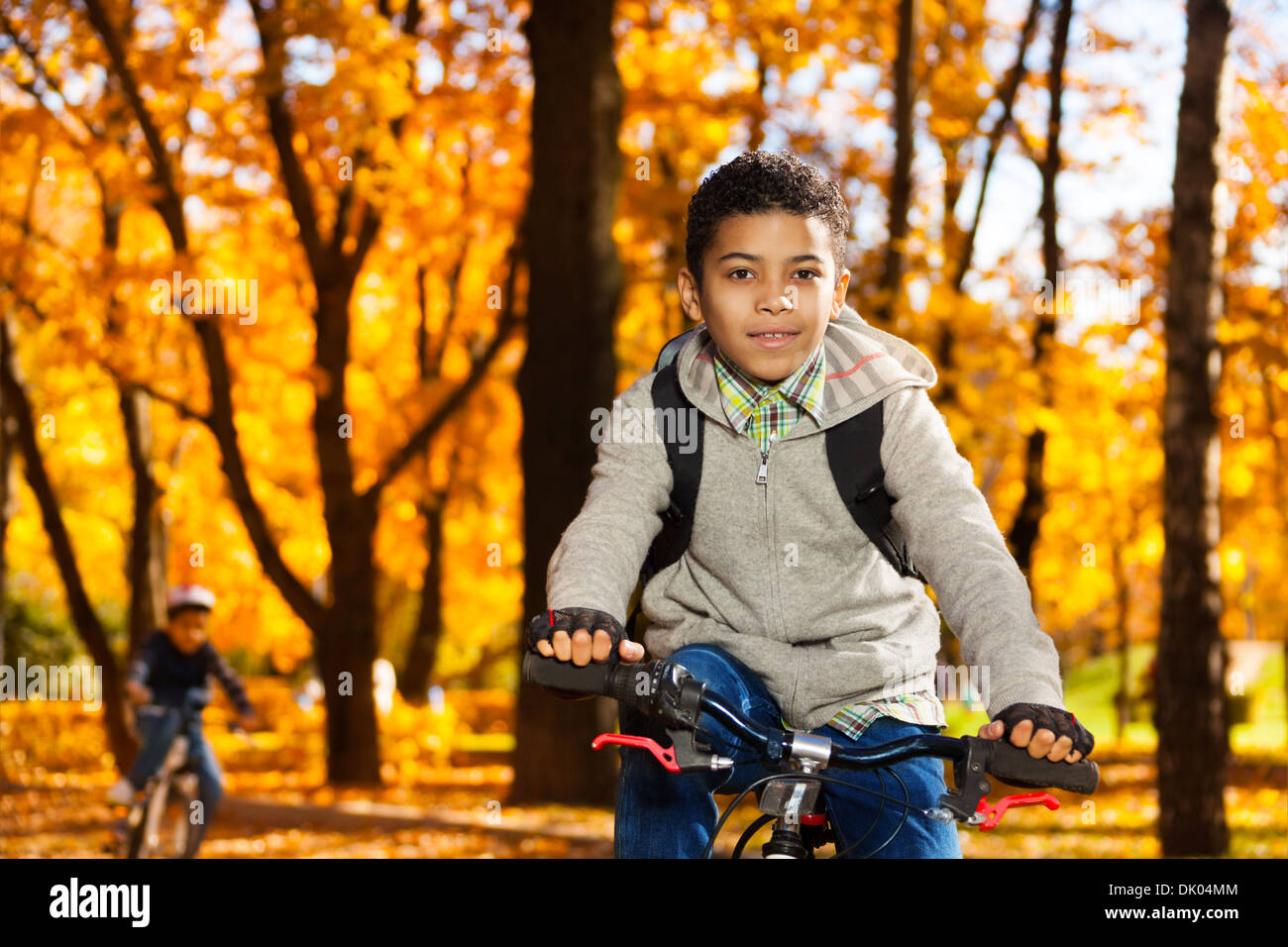 Close portrait of a boy on the bicycle riding in autumn park with orange leaves Stock Photo