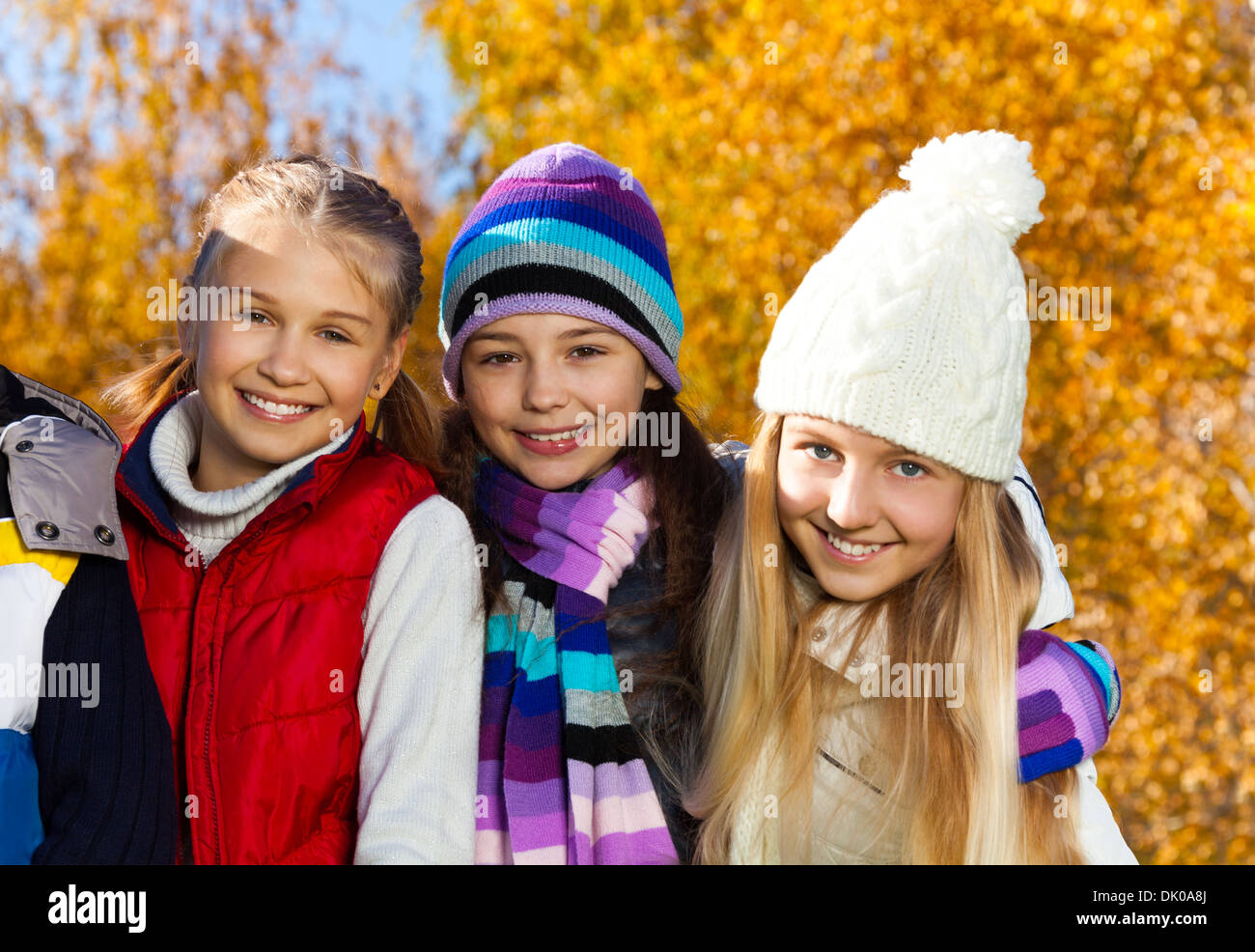 Close portrait of three happy kid, girls girls in autumn clothes on sunny day with happy smiling faces wearing warm clothes Stock Photo
