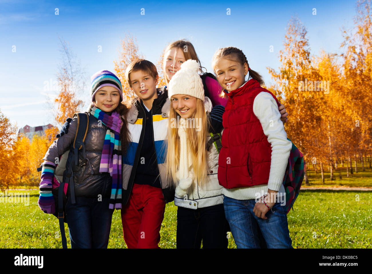Group of five happy kids, boys and girls standing in the park after school wearing warm clothes on sunny autumn day Stock Photo