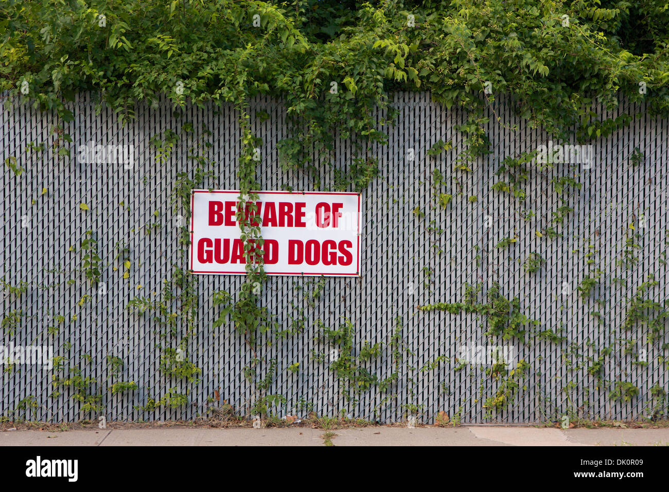 Warning sign reading 'Beware of Guard Dogs' mounted on an overgrown fence. Stock Photo