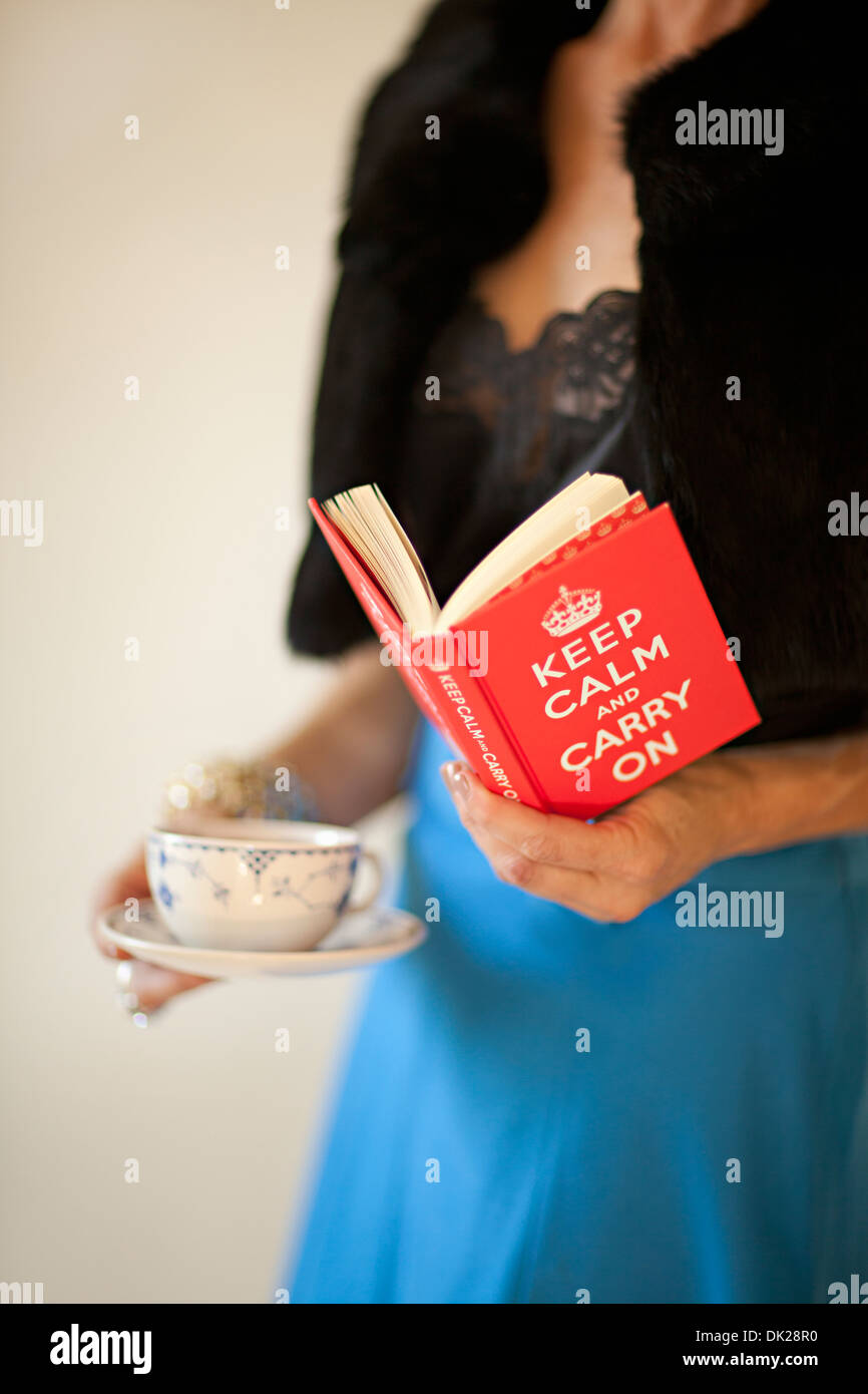 Close up midsection of well-dressed woman holding teacup and reading ‘Keep Calm and Carry On’ book Stock Photo