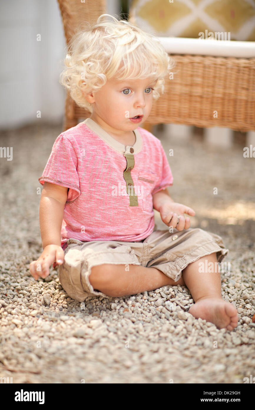 Surprised Blonde Toddler Boy With Curly Hair Playing In Pebbles On