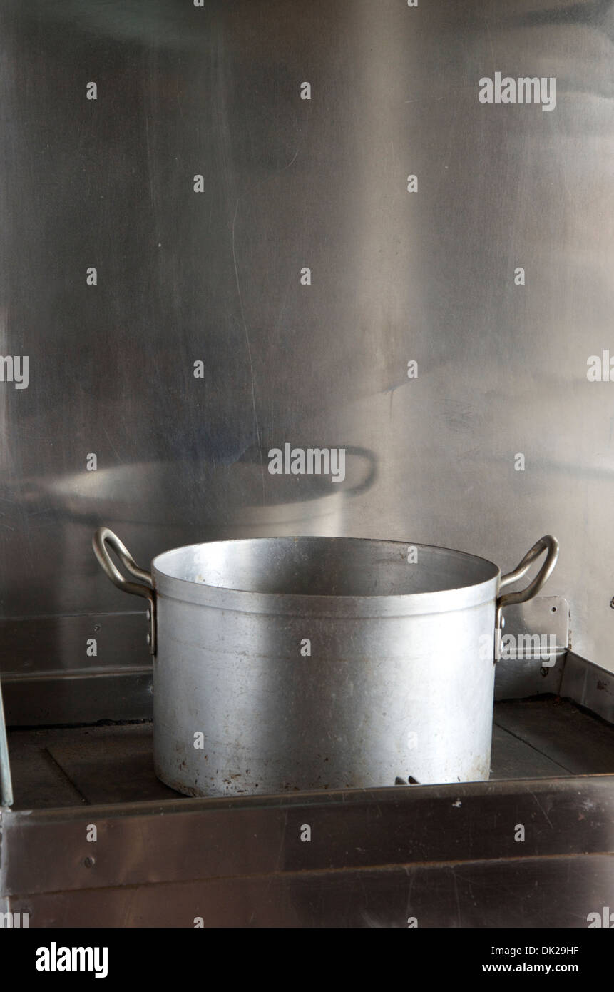 Large empty stainless steel catering pan sitting on industrial hob reflected in stainless steel back panel Stock Photo