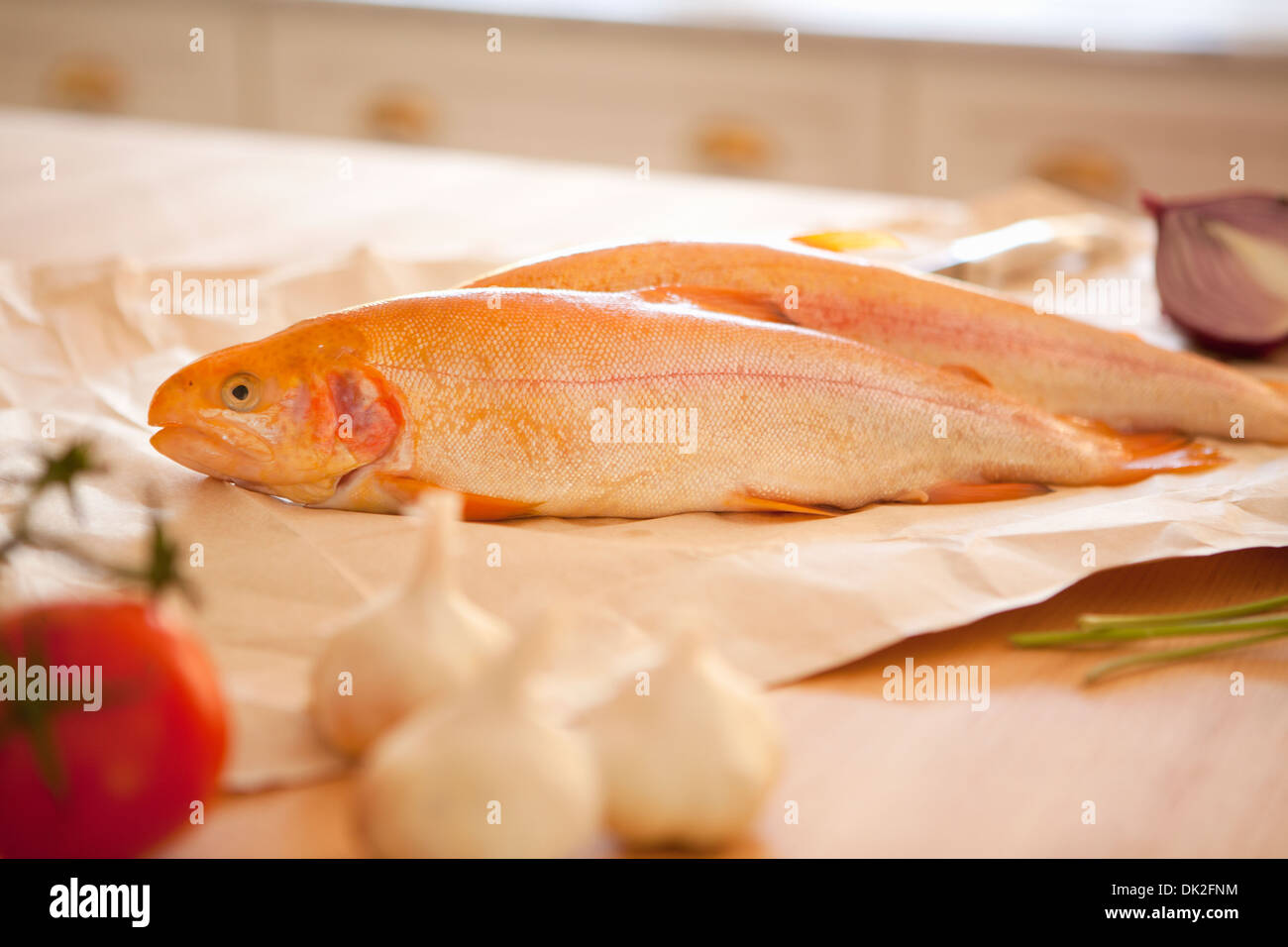 Close up of whole fish, garlic and tomato ingredients on kitchen counter Stock Photo