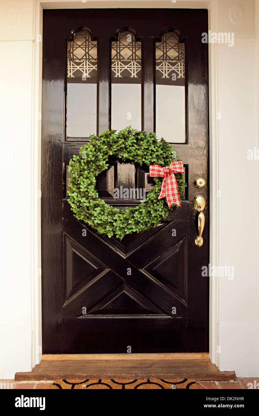 Red and white gingham ribbon on Christmas wreath hanging from black front door Stock Photo
