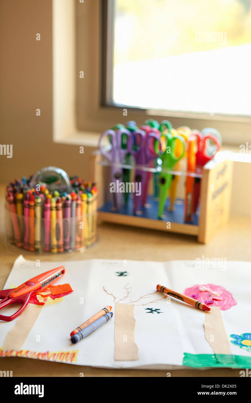 Child’s art crayons and scissors at drawing near window Stock Photo