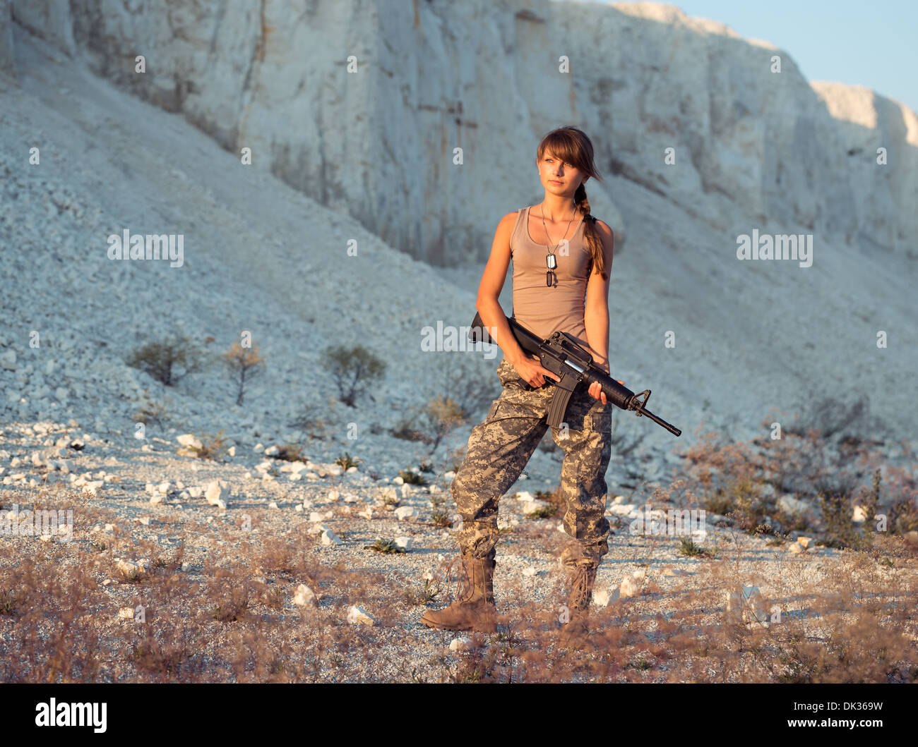 Young beautiful female soldier dressed in a camouflage with a gun in the location Stock Photo