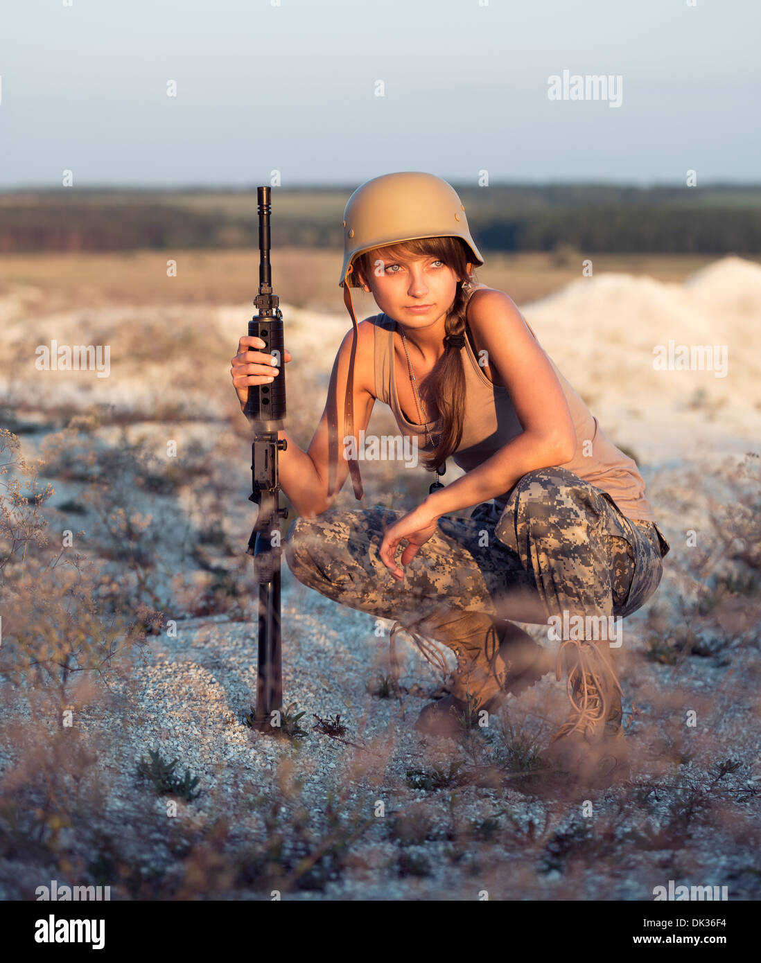 Young beautiful female soldier dressed in a camouflage with a gun in the outdoor Stock Photo