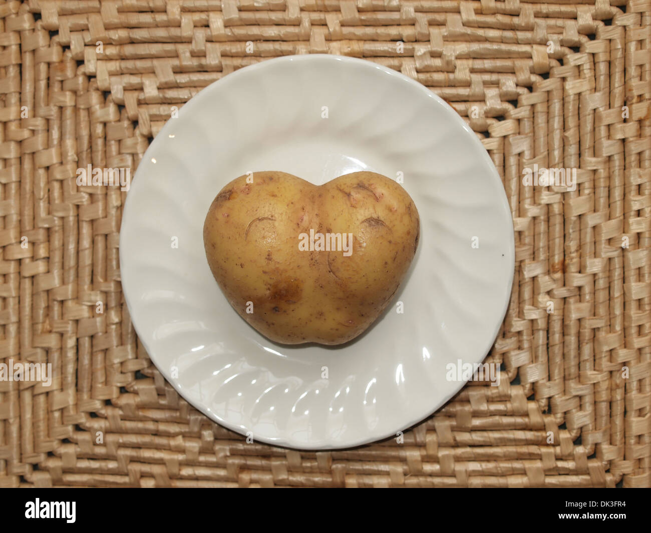Organic Heart Shaped Potato on a plate on a natural woven mat. Love your food. Stock Photo