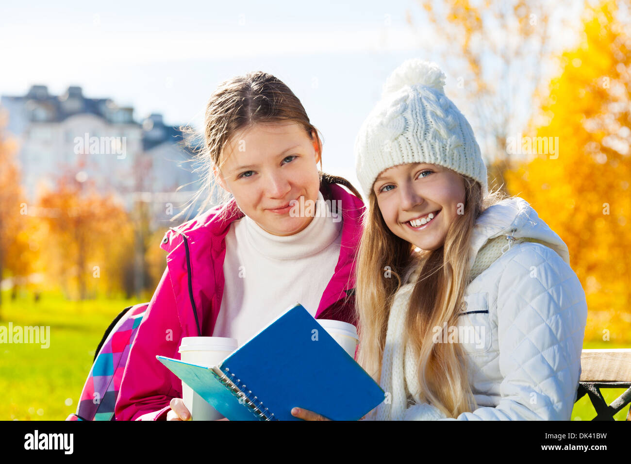 Close portrait of two happy 14 years old girls in the autumn park with textbook and coffee smiling and looking at camera Stock Photo