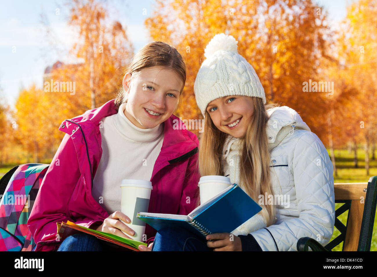 Close portrait of two happy 14 years old girls in the autumn park with textbook and coffee laughing and looking at camera Stock Photo