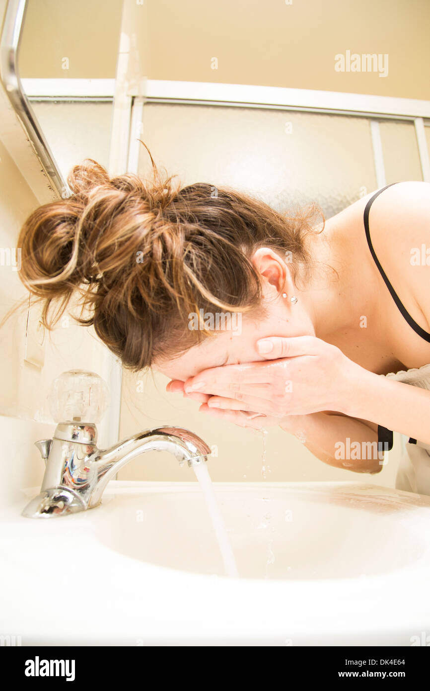 Young woman in nightgown washing face in bathroom sink Stock Photo