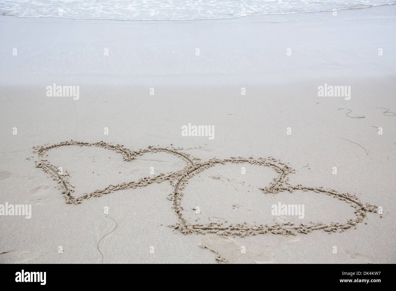 Two hearts carved into wet sand Stock Photo