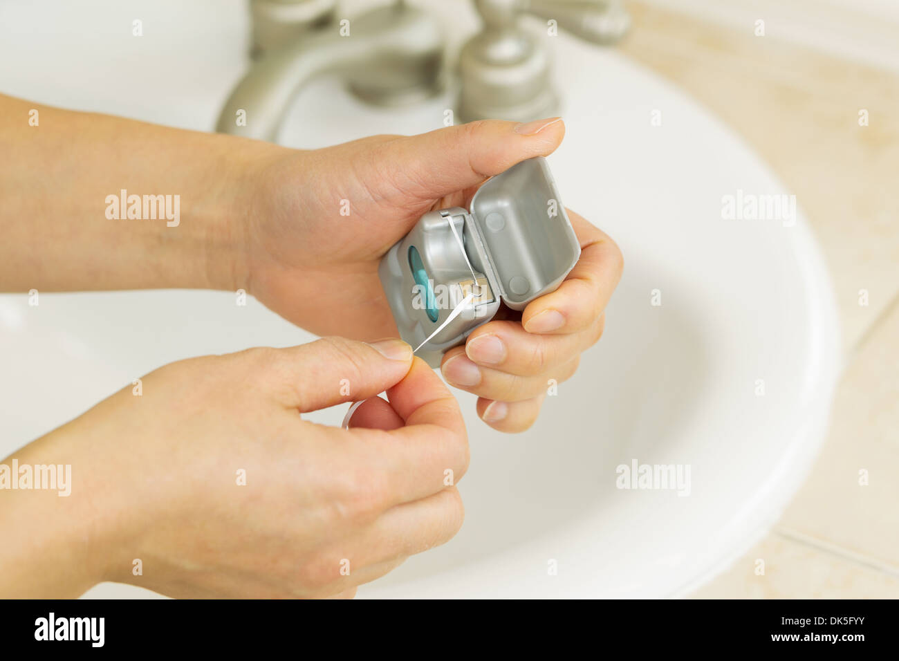 Horizontal photo of female hands pulling dental floss out of small
