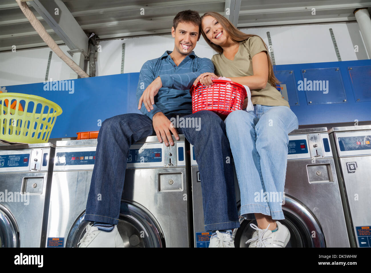 Couple With Clothes Basket Sitting On Washing Machine Stock Photo