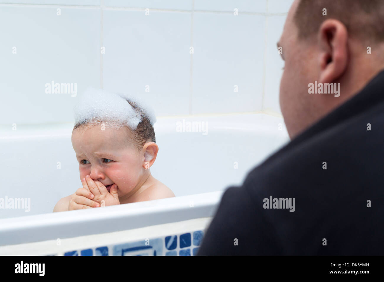 Sad baby boy crying in bath and detail of his daddy. Stock Photo