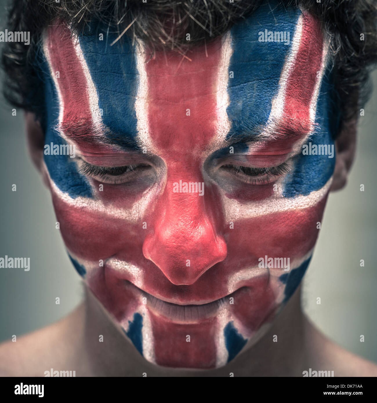 Closeup of smiling man with British flag painted on face looking down. Stock Photo