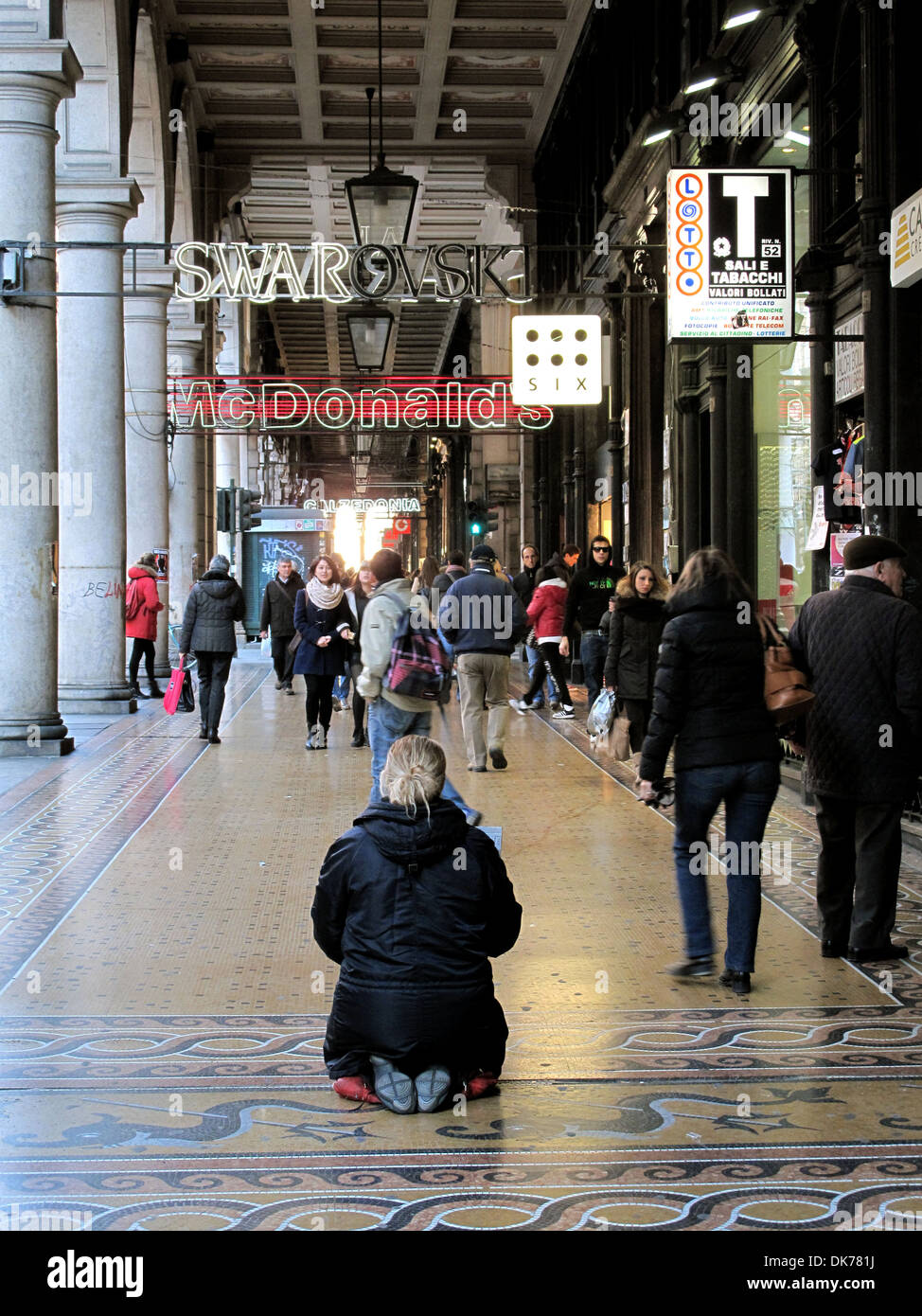 A homeless woman kneeling on a mosaic pavement in an arcade along Via XX Settembre in Genoa. Stock Photo