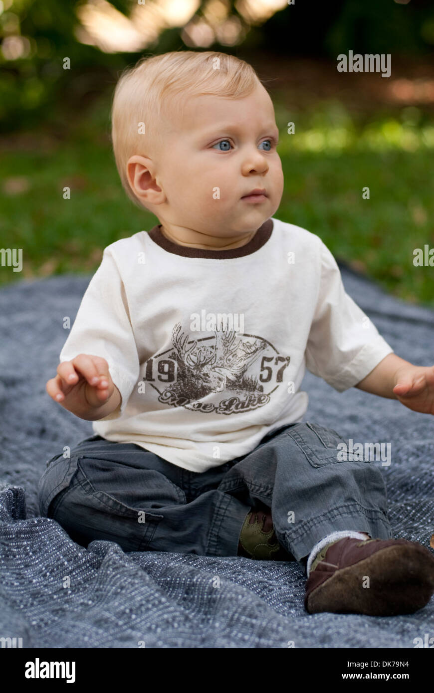 A baby boy sits on a blanket outside. Stock Photo