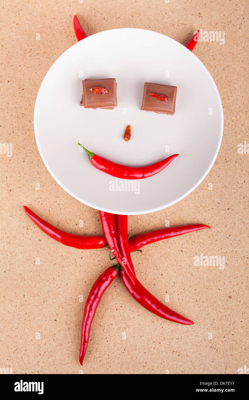 Happy chili pepper character with chocolate eyes on plate, over wooden