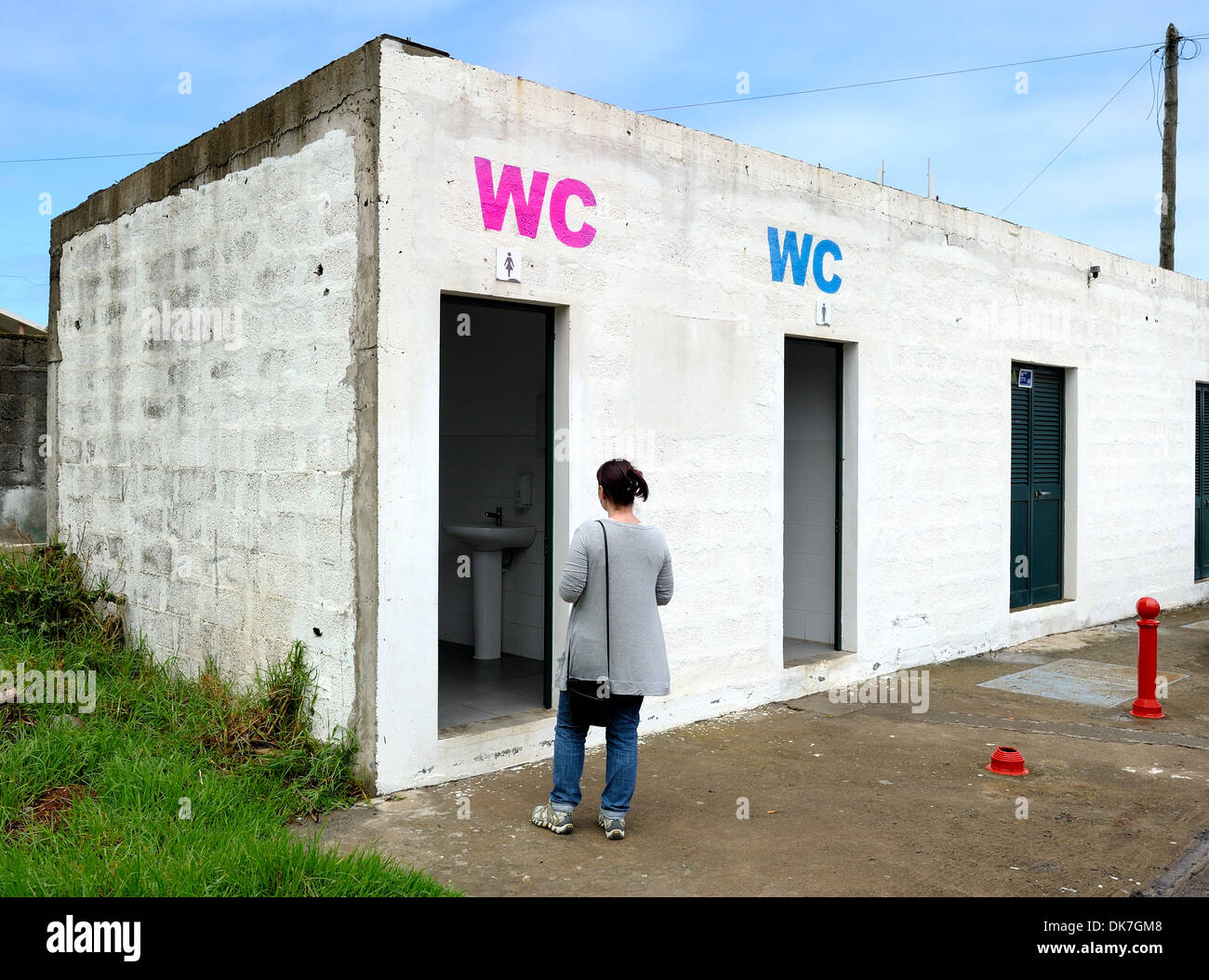 Porto Moniz Madeira Portugal. A woman waits outside the female toilet of a car park toilet block. Stock Photo